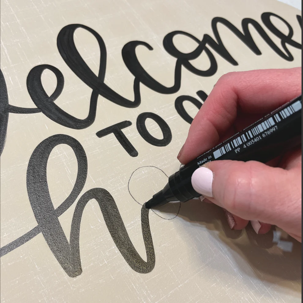 Hand lettering "Welcome to our home" with a black lettering pen on a white door hanger